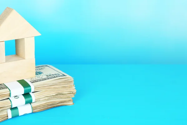 Dom drewniany na opakowaniach dolarów na niebieskim tle — Zdjęcie stockowe