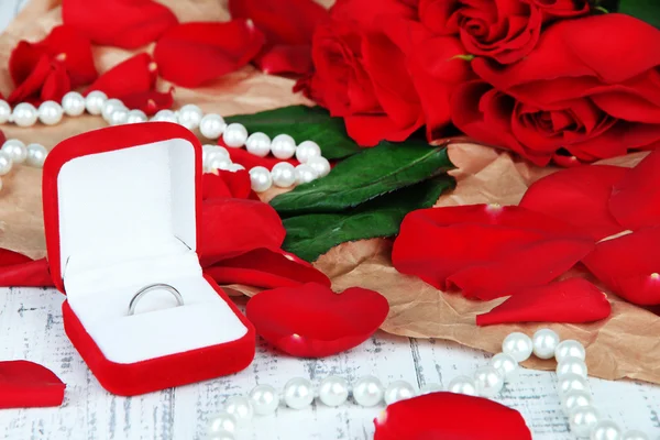Ring umgeben von Rosen und Blütenblättern auf Holztisch in Großaufnahme — Stockfoto