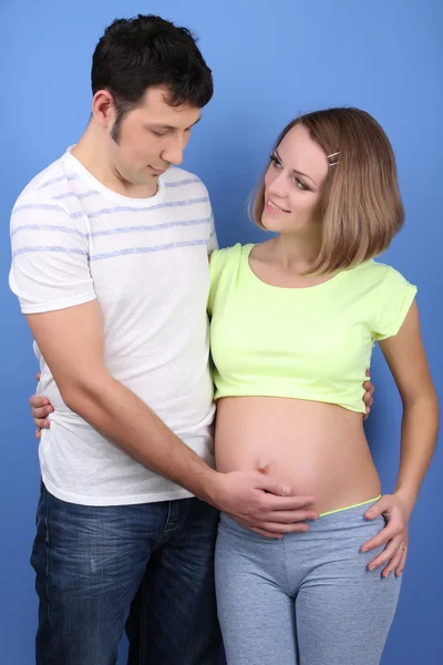 年轻孕妇和她的丈夫在蓝色背景上 — 图库照片