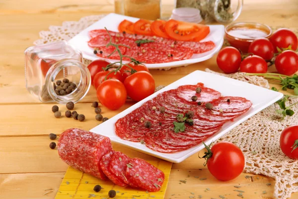 Leckere Salami auf Tellern auf Holztisch in Großaufnahme — Stockfoto