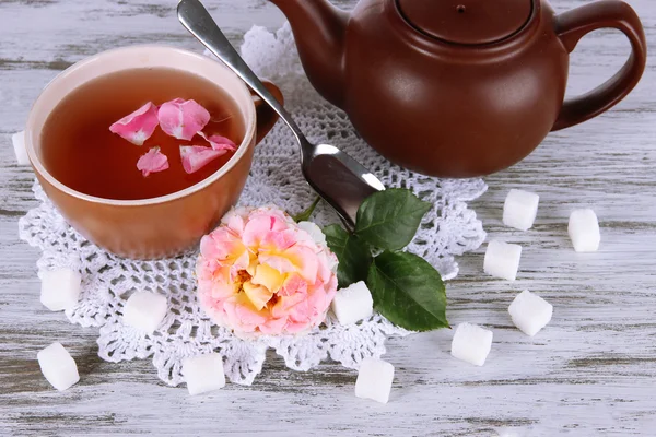 Waterkoker en kopje thee uit de thee rose aan boord op servet op houten tafel — Stockfoto