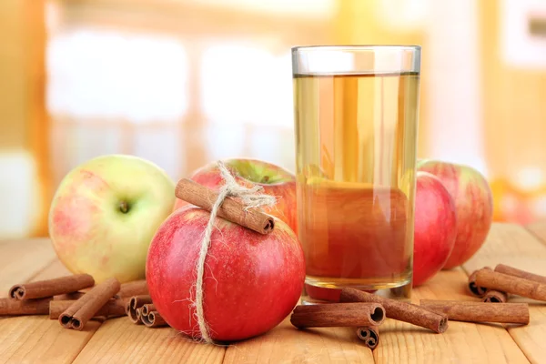 Ripe apples with with cinnamon sticks and glass of apple drink on wooden table, on bright background — Stock Photo, Image