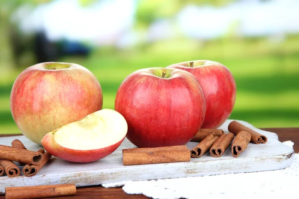 Ripe apples with with cinnamon sticks on wooden table, on bright background — Stock Photo, Image