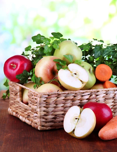 Zoete appelen en wortelen in mand op houten tafel op natuurlijke achtergrond — Stockfoto