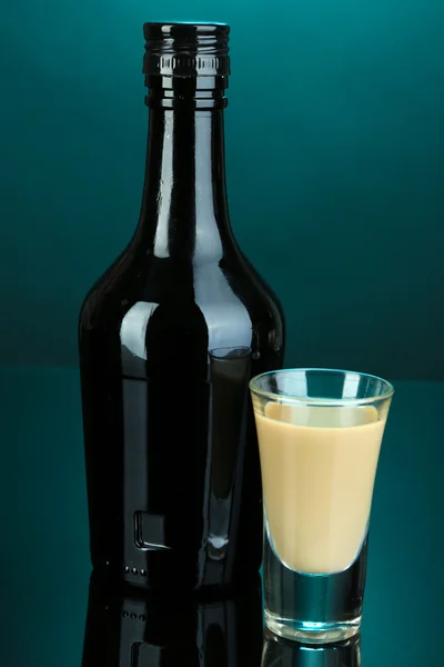 Licor Baileys en botella y vidrio sobre fondo azul — Foto de Stock