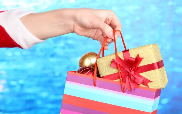 Hand hält Paket mit Neujahrsbällen und Geschenken auf blauem Hintergrund — Stockfoto