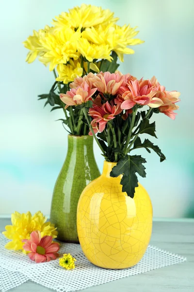 Beautiful flowers in vases, on wooden table, on light background — Stock Photo, Image