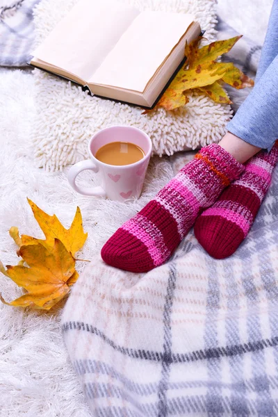 Composizione con plaid caldo, libro, tazza di bevanda calda e gambe femminili, su sfondo tappeto di colore — Foto Stock