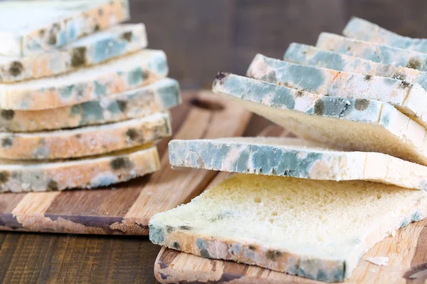 Mouldy bread on cutting board, on wooden background — Stock Photo, Image