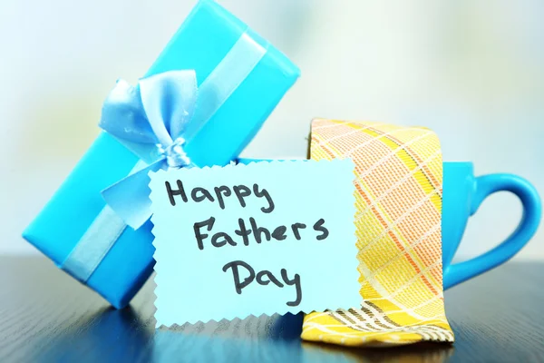 Happy Fathers Day tag with gift boxes, cup and tie, on wooden table, on light background — Stock Photo, Image