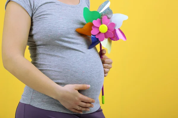 Mujer embarazada sosteniendo molino de viento de colores sobre fondo amarillo — Foto de Stock