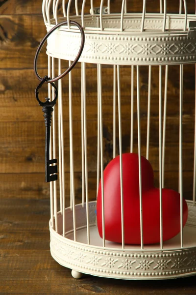 Heart in decorative cage on wooden background — Stock Photo, Image