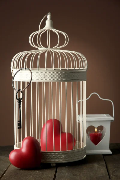 Hearts in decorative cage on wooden table, on brown background — Stock Photo, Image