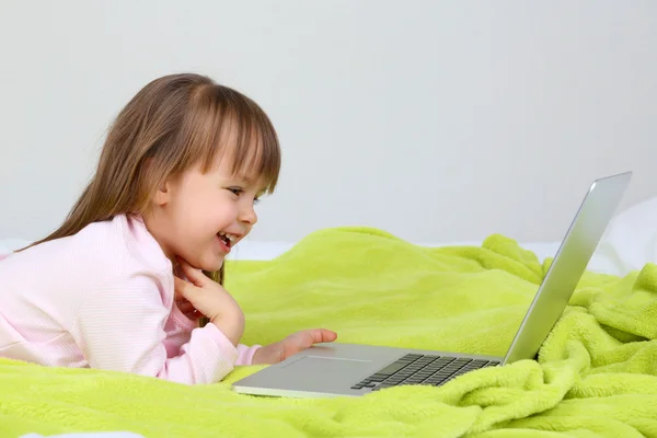 Niña con portátil en la cama en el fondo de la pared —  Fotos de Stock