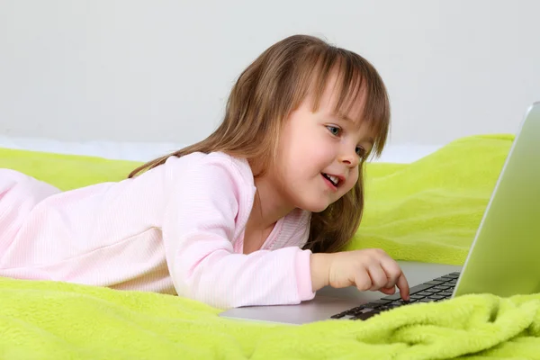 Niña con portátil en la cama en el fondo de la pared — Foto de Stock