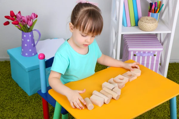 Little girl plays with construction blocks sitting at table in room — Stock Photo, Image