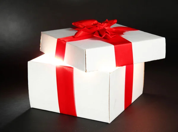 Gift box with bright light on it on dark grey background — Stock Photo, Image