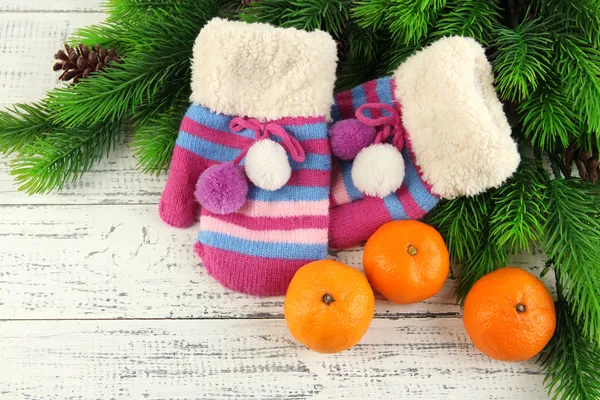 Striped mittens with fir branches and tangerines on wooden background — Stock Photo, Image