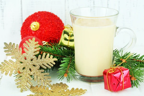 Cup of eggnog with fir branches and Christmas decorations on table on wooden background — Stock Photo, Image