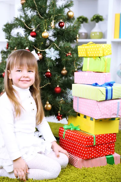 Liten flicka med presenterar nära julgran i rum — Stockfoto