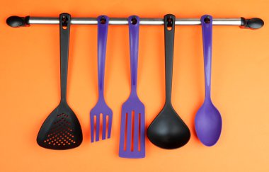 Turuncu arka planda gümüş kancalarda plastik mutfak aletleri.