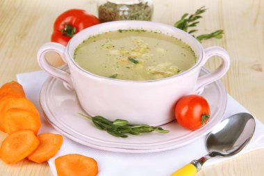 Nourishing soup in pink pan with ingredients on wooden table close-up