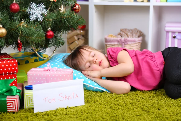 Kleines Mädchen schläft neben Weihnachtsbaum im Zimmer — Stockfoto
