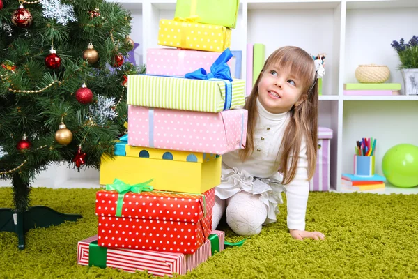 Liten flicka med presenterar nära julgran i rum — Stockfoto