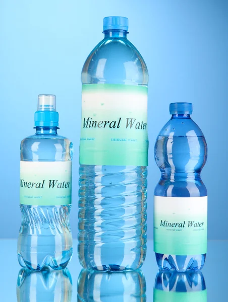 Diferentes botellas de agua con etiqueta sobre fondo azul — Foto de Stock