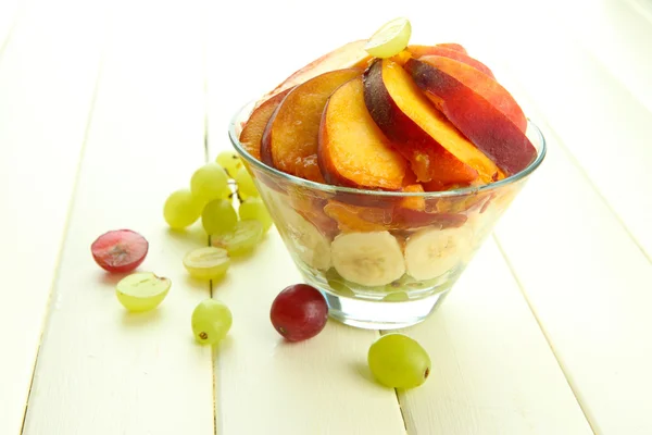 Salade de fruits savoureuse dans un bol en verre, sur une table en bois blanc — Photo