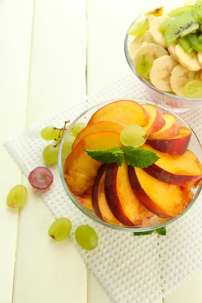 Smakelijke fruitsalade in glazen kommen, op witte houten tafel — Stockfoto