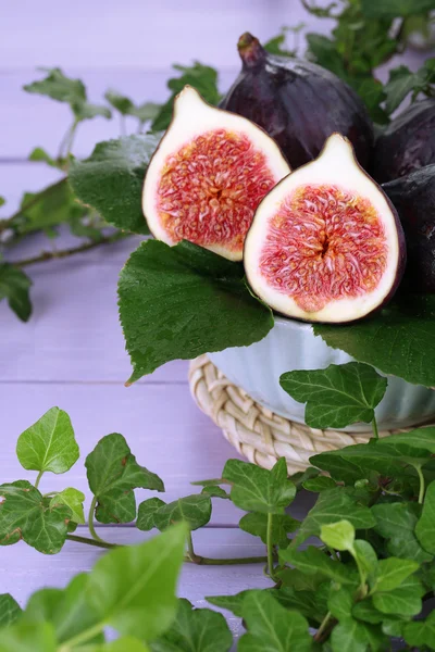 Ripe figs in bowl in leaves on wooden table close-up — Stock Photo, Image