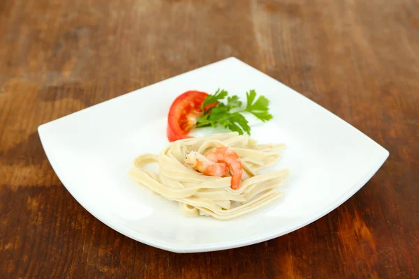 Pasta met garnalen op witte plaat, op houten achtergrond — Stockfoto