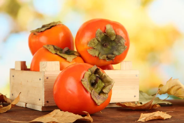 Ripe persimmons in crate on table on bright background — Stock Photo, Image