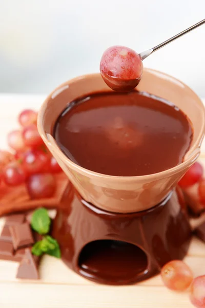 Chocolade fondue met fruit, op houten tafel, op lichte achtergrond — Stockfoto