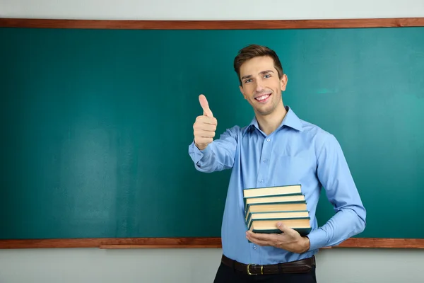 Young teacher with books near chalkboard in school classroom — Stock Photo, Image