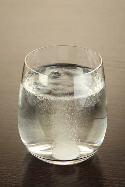 Glass with efervescent tablet in water with bubbles on wooden table — Stock Photo, Image