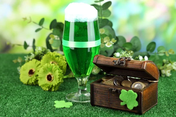 Glass of green beer and pitcher with coins on grass close-up — Stock Photo, Image