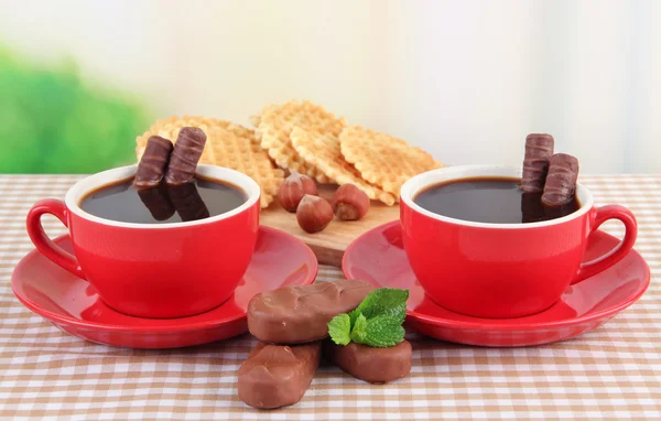Copos vermelhos de café forte com barras de chocolate e waffles na toalha de mesa em fundo brilhante — Fotografia de Stock