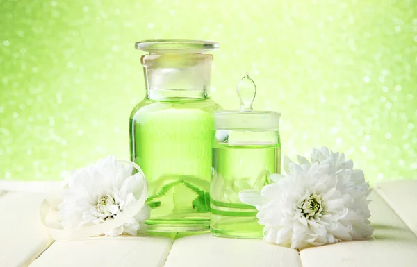 Botellas de vidrio con esencia de color, sobre mesa de madera, sobre fondo verde —  Fotos de Stock