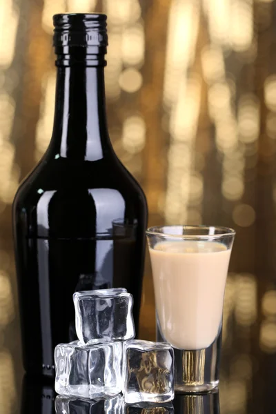 Baileys liqueur in bottle and glass on golden background — Stock Photo, Image