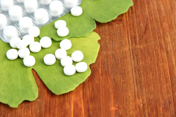 Листья гинкго билоба и таблетки на деревянном фоне — стоковое фото