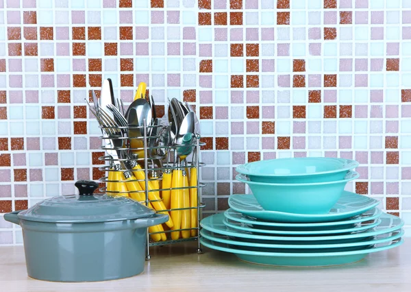 Dishes and cutlery in kitchen on table on mosaic tiles background — Stock Photo, Image