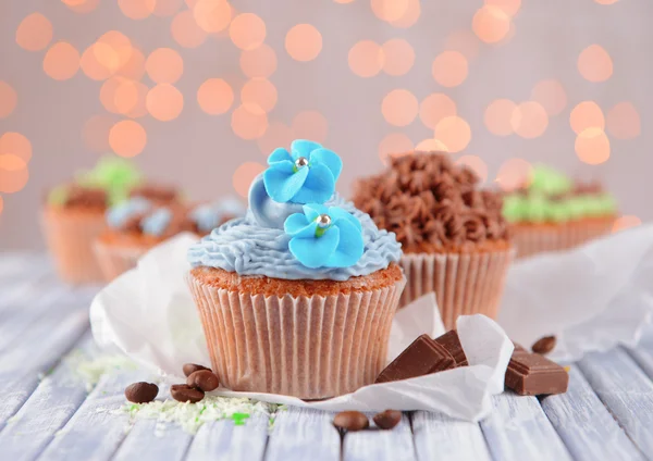 Leckere Cupcakes mit Buttercreme, auf farbigem Holztisch, auf Lichtern Hintergrund — Stockfoto
