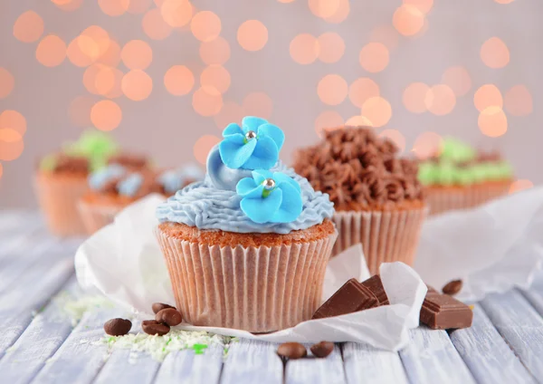 Tasty cupcakes with butter cream, on color wooden table, on lights background — Stock Photo, Image