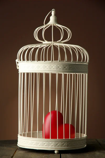 Heart in decorative cage on wooden table, on brown background — Stock Photo, Image