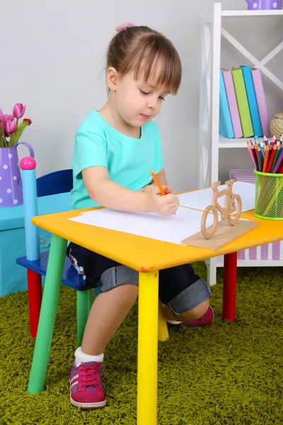 Маленька дівчинка малює, сидячи за столом в кімнаті — стокове фото