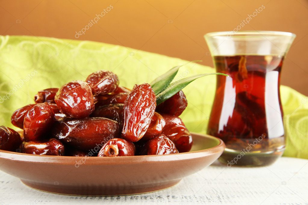 Dried dates on plate with cup of tea on table on fabric background