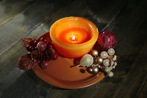 Burning candle with Christmas decorations on color plate, on wooden background — Stock Photo, Image
