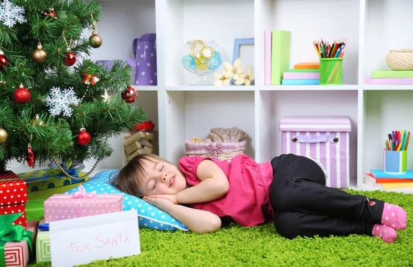 Klein meisje slaapt in de buurt van de kerstboom op kamer — Stockfoto